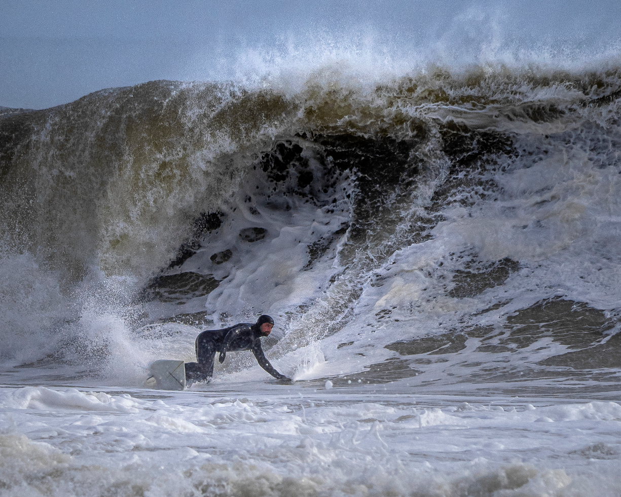 A surfer crouches on a board as a large wave breaks behind him